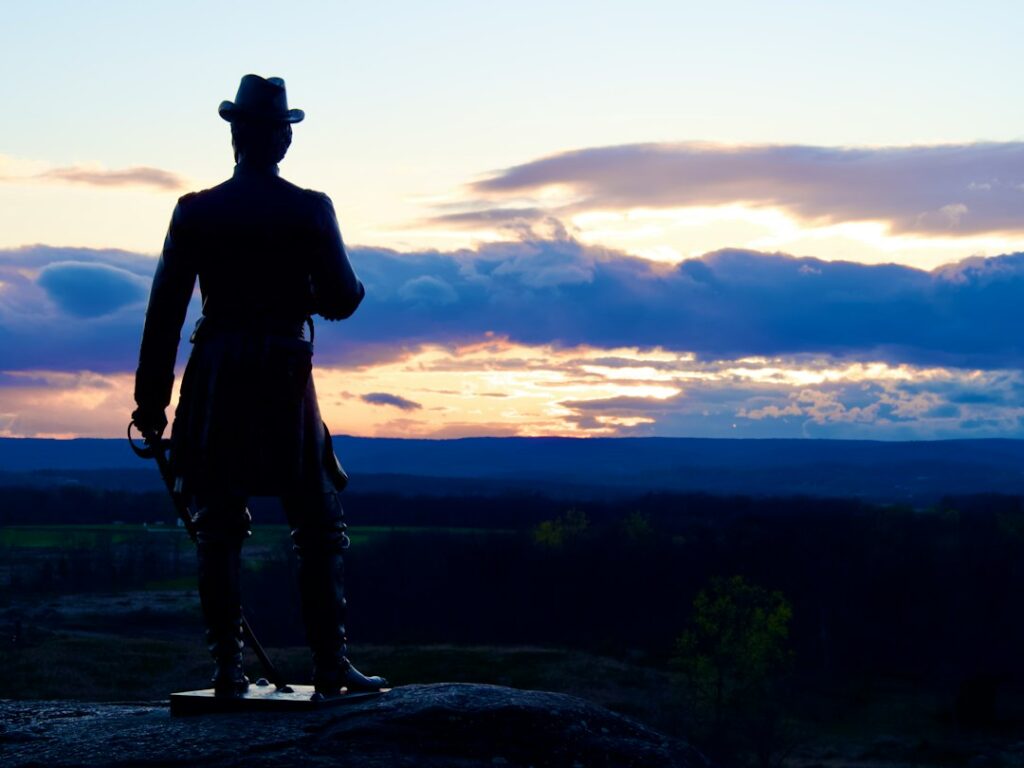 A statue silhouette overlooks a landscape at sunset.